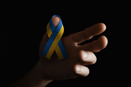 wearing a yellow and blue ribbon on the finger, on dark background.. concept needs help and support, truth will win