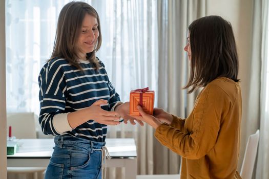 Young girl gives a nice wrapped gift to her friend, a woman makes a pleasant surprise for an anniversary, present for birthday or new year, christmas. People celebrate and congratulate each other.