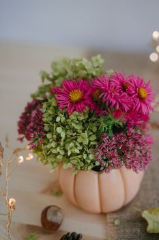 Autumn composition with a bouquet of flowers in a vase in the form of an orange pumpkin. Autumn room decor. Garland with warm light. Bokeh. Thanksgiving Day. Festive composition.