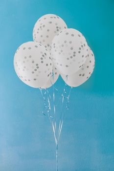 White helium balloons with gray dots on blue background. Several white and gray spotted holiday balloons on metal ribbons against blue painted wall that looks like clear sky. Birthday present
