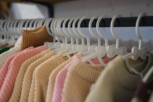 Clothing store. Sweaters on hangers in the store. Sale of warm clothes. Children's sweaters. Knitted sweaters in pink, beige and white.