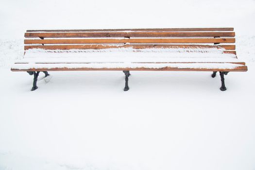 On a winter day in the park. Wooden bench covered with snow. A bench in the park after a snowfall. Winter time, weather phenomenon.