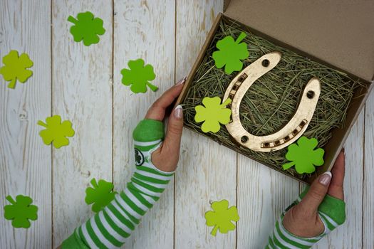 Women's hands hold a box with a gift for St. Patrick's Day. Horseshoe in a craft box filled with fresh hay. Background.