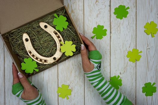Women's hands hold a box with a gift for St. Patrick's Day. Horseshoe in a craft box filled with fresh hay. Background.