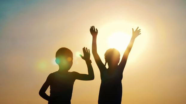 Silhouettes, figures of children, boy and girl jumping, having fun, dancing, hugging against the background of the sun, at sunset in summer. Happy family. Slow motion. High quality photo