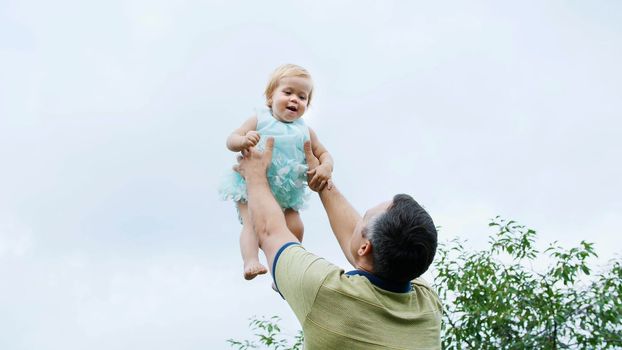 summer, in the garden, mother, a view from below, the daddy throws his one-year-old daughter, plays with her, has fun. She is laughing. family spends their leisure time together. High quality photo