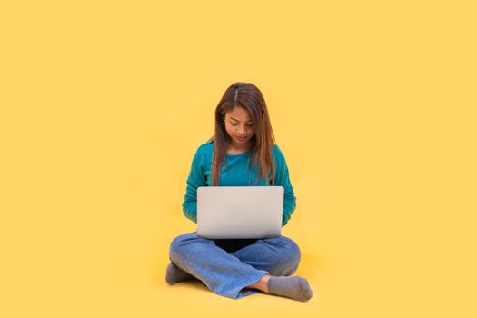 Full body young latin woman 20s on floor work on laptop isolated on yellow background studio. High quality photo