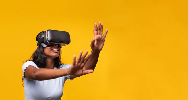 Young indian woman wearing virtual reality simulator gesturing on yellow background. Horizontal banner. Technology concept.