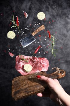 Art photo levitation of a meat steak with ingredients for frying oil spices rosemary pepper garlic on a gray background. High quality photo