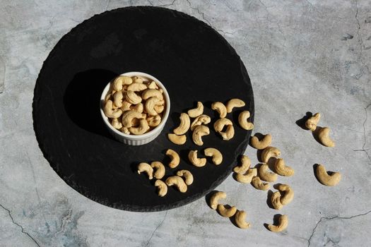 Cashew nuts on the black stone plate on the grey cement background. Top view.