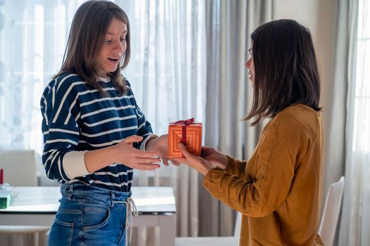 Young girl gives a nice wrapped gift to her friend, a woman makes a pleasant surprise for an anniversary, present for birthday or new year, christmas. People celebrate and congratulate each other.