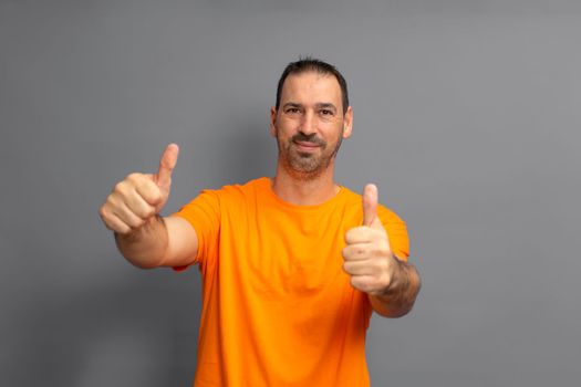 Attractive cheerful hispanic man with a beard wearing t-shirt standing isolated over gray background, showing thumbs up