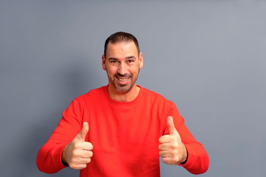 Attractive cheerful latino man with a beard standing isolated over gray background, showing thumbs up