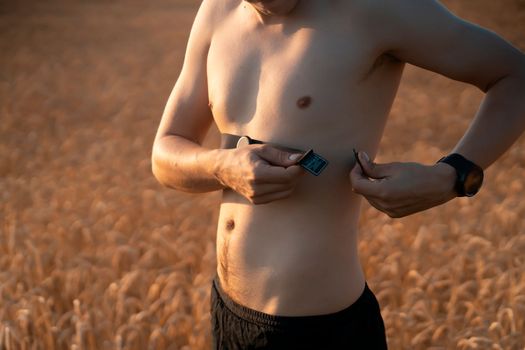 An athletic young man warms up outdoors, puts on a heart rate monitor and prepares for an active run, a person leads a healthy lifestyle and competently approaches running training.