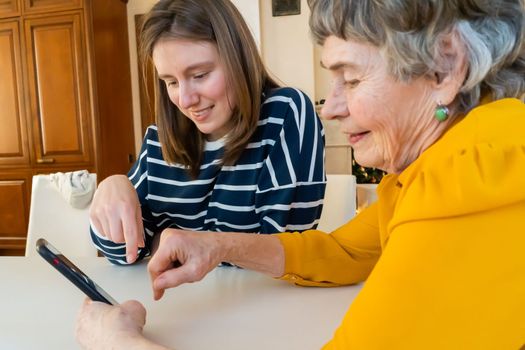 Young girl, a granddaughter, explains to an elderly relative how to use a smartphone and an application to communicate with a doctor at home. The family loves and cares for their elderly parents.