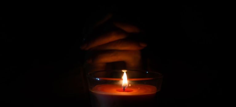 a woman warms her hands on a burning candle.