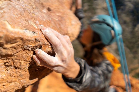 Young girl is engaged in extreme sports, fearlessly climbs up the rock using white magnesia powder, holds her hand to the ledge in the relief, close-up view, focus on the finger, the girl is blurred.