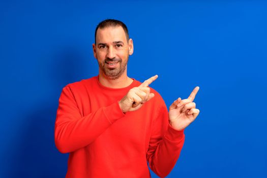 Hispanic man with beard pointing index fingers to the side in copy space mock up isolated on blue colored background studio portrait
