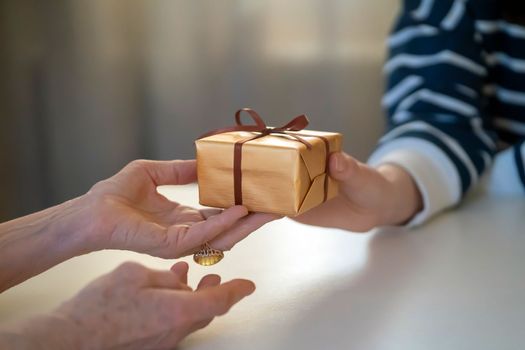 Female hands hold a gift closeup, top view. A young girl gives a nice packed surprise to her mother, grandmother with love, remembers elderly relatives, visits during holidays, takes care of them.