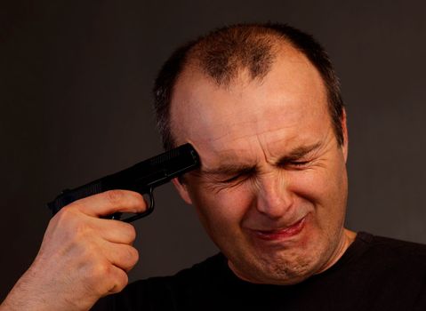 The man put a gun to his head. A close-up studio portrait of a man 40-50 years old trying to shoot himself with a pistol.