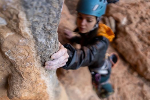 Young girl is engaged in extreme sports, fearlessly climbs up the rock using white magnesia powder, holds her hand to the ledge in the relief, close-up view, focus on the finger, the girl is blurred.