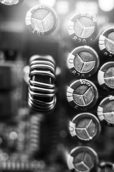 Black and white background of various electronic components on a printed circuit board close-up. Ferrite core of the inductor, wrapped with copper wire, resistors and capacitors on the printed circuit board. The concept of electro and microprocessor technologies. Selective focus. Vertical photo