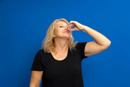 Pretty caucasian blonde woman in a black t-shirt shows a perfect gourmet delicious sign isolated on a blue colored background