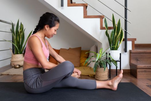 Young Asian woman warming up joints before yoga practice at home. Active lifestyle concept.