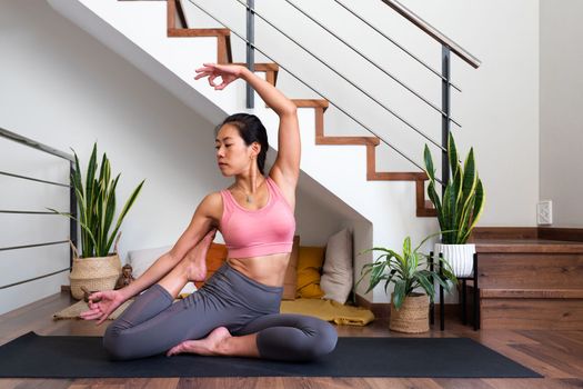 Young flexible Asian woman doing beautiful yoga asana at home living room. Healthy lifestyle concept.