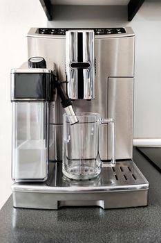 Steel-colored coffee machine for making different types of coffee with glass cup on stand. Preparation for making coffee
