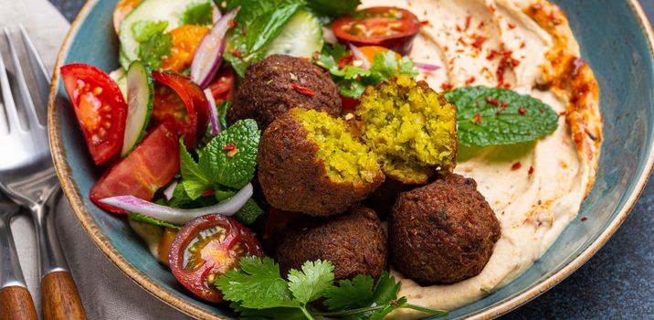 Close up of Middle Eastern Arab meal with fried falafel, hummus, vegetables salad with fresh green cilantro and mint leaves on ceramic plate on stone rustic background table. Arabic traditional cuisine