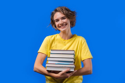 Clever student woman holds stack of university books from college library on blue background. Happy girl smiles, she is happy to graduate. High quality photo