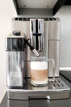 Cappuccino coffee in glass cup stands on stand of coffee machine, close-up