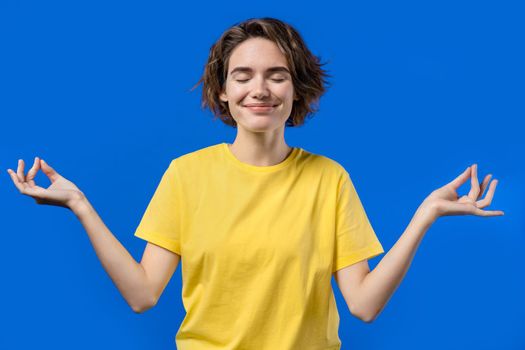 Calm woman relaxing, meditating, refuses stress. Sunny girl breathes deeply, calms down blue studio background. Yoga, moral balance, zen concept. High quality photo