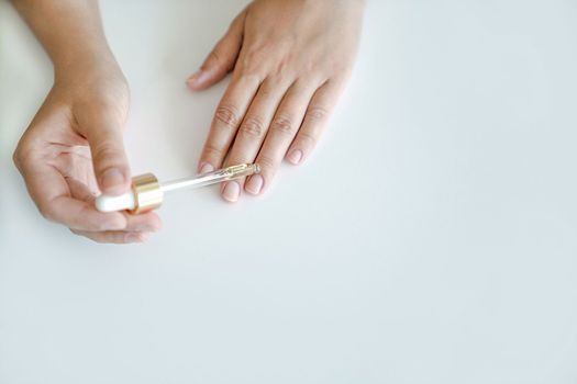 Nail and hand skin care. Woman holds pipette with oil to apply to her nails for treatment and strengthening of nails. Hands close-up, no face, copy space