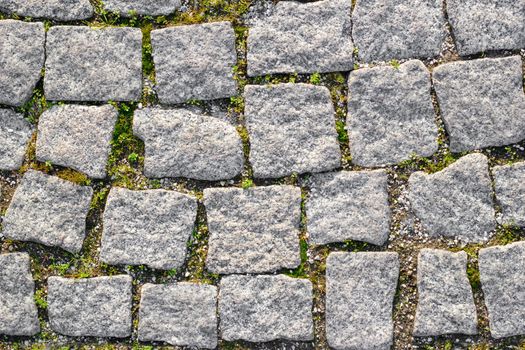 Texture of paved stone road with sprouted grass between masonry. Top view
