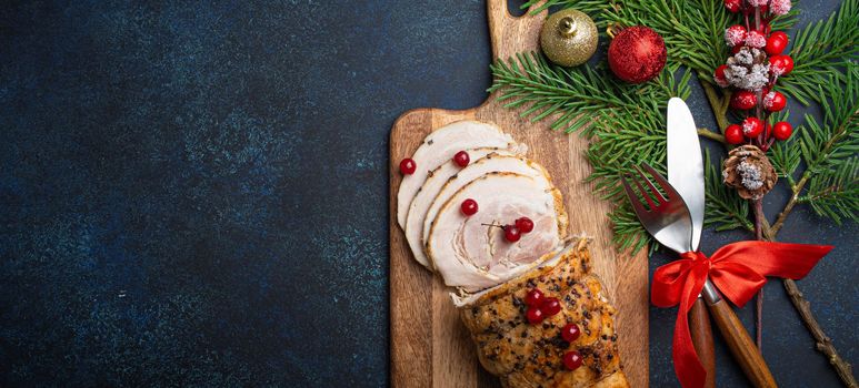 Christmas baked ham sliced with red berries and festive decorations on wooden cutting board, dark rustic background from above. Christmas and New Year holiday dinner with baked pork, space for text