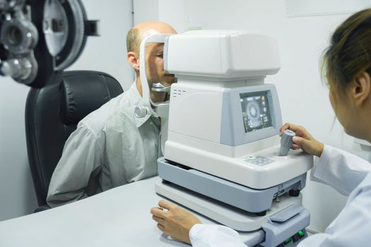 Smart handsome man sitting in optometrist cabinet having his eyesight checking, examining, testing with special equipment machine by professional optician for new pairs of eyeglasses.