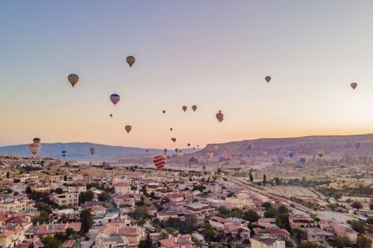 Colorful hot air balloons flying over at fairy chimneys valley in Nevsehir, Goreme, Cappadocia Turkey. Spectacular panoramic drone view of the underground city and ballooning tourism. High quality.