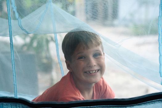 Smile child boy lie rest hammock with mosquito net. Happy childhood daydream. Look at from, laughing, portrait.