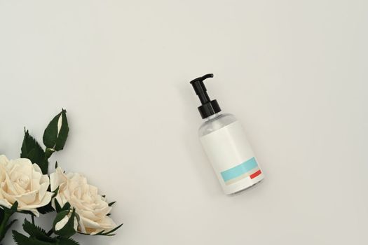 Shampoo or soap plastic bottle dispenser with white rose on white background. Natural skincare, beauty product design concept.