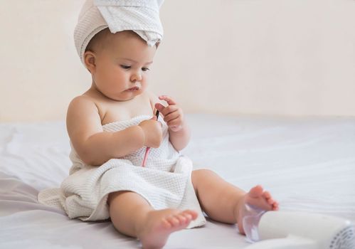 beautiful baby with a white towel on her head looks at eyeliner for eyelids on the bed