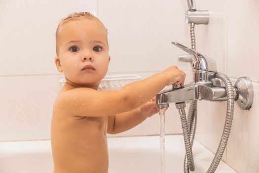 Baby bathes in the bathroom holding on to the water tap.