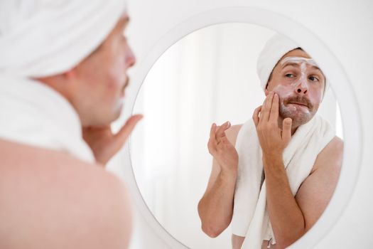 Mature man looking in mirror touch his face after shave applied aftershave cream enjoy smooth, flawless, soft skin.