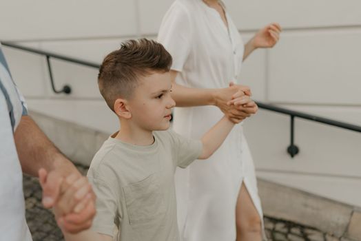 A close photo of a boy who is holding the hands of his mother and father while descending the stairs of the palace in an old European town.