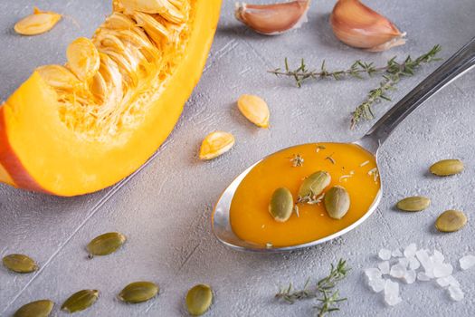 Pumpkin puree soup with pumpkin seeds and thyme in a spoon and a piece of ripe pumpkin. Healthy diet. Selective focus.