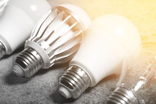 Incandescent lamp and various LED lamps with e27 base on gray background with light flare.