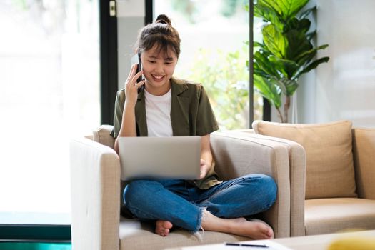 Young asian businesswoman uses a mobile phone to contact a customer, working hard at the office using laptop data graphs, planning for improvement, analyzing and strategizing for business growth. Business concept
