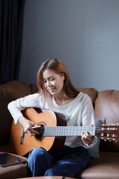 Portrait of young asian woman playing guitar on sofa relaxing stress on vacation.