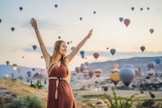 Tourist woman looking at hot air balloons in Cappadocia, Turkey. Happy Travel in Turkey concept. Woman on a mountain top enjoying wonderful view.